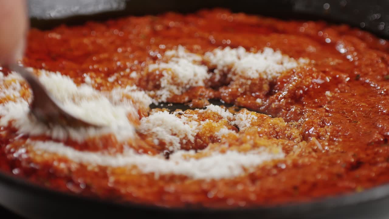 Adding grated cheese Parmesan to tomato sauce close-up. Cooking classic homemade Italian tomato sauce for pasta and pizza in the pan. Chef cooking traditional Italian food. High quality 4k footage