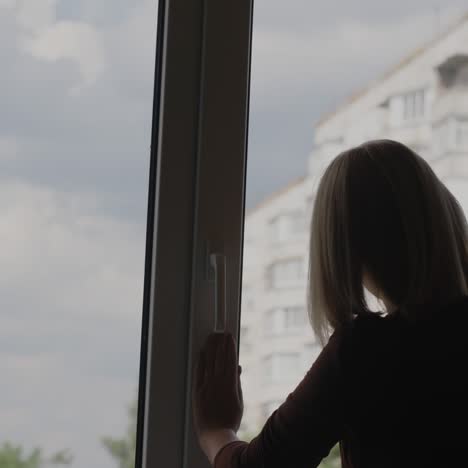 a woman washes a window in the apartment of a high-rise building