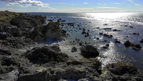 Aerial-view-of-Rauk,-rock-formations,-on-the-shoreline-of-Faro-island,-sun-glimpsing-on-the-sea-surface,-on-a-tranquil,-summer-day,-in-Gotland,-Sweden---static,-drone-shot