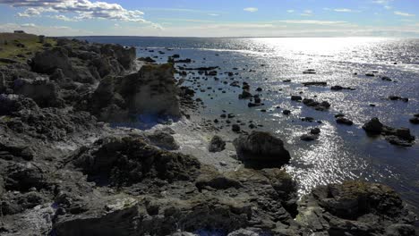 vista aérea de rauk, formaciones rocosas, en la costa de la isla de faro, sol vislumbrando en la superficie del mar, en un tranquilo día de verano, en gotland, suecia - estática, disparo de drones