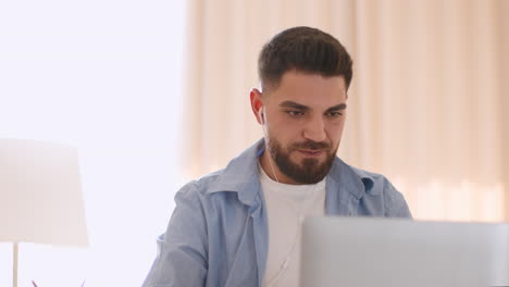 bearded man working on laptop with earbuds