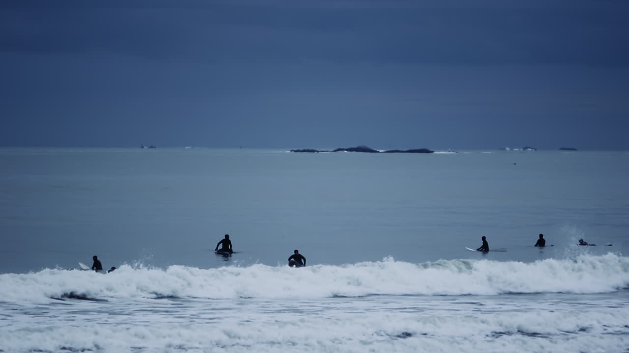 Silhouettes of many people having fun surfing on atlantic ocean in a cloudy day. Nantasket Beach in Hull, MA USA
