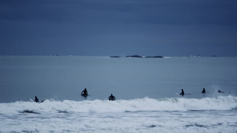 silhouettes of many people having fun surfing on atlantic ocean in a cloudy day. nantasket beach in hull, ma usa
