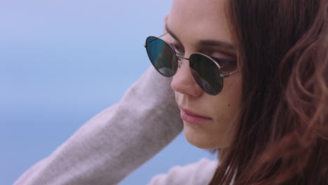 retrato de una hermosa mujer caucásica con gafas de sol disfrutando de una tranquila playa al atardecer buscando contemplativa corriendo la mano a través del cabello