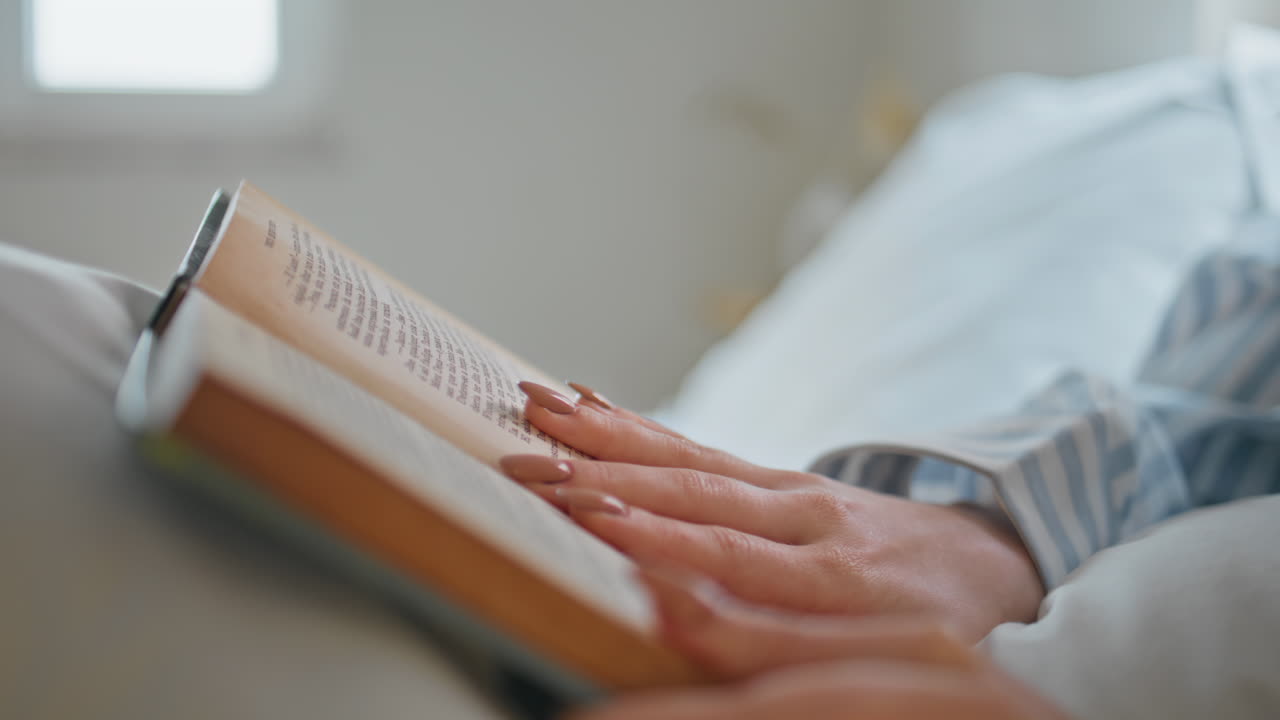 Reader hands touching book in serene bedroom setting closeup. Woman reading