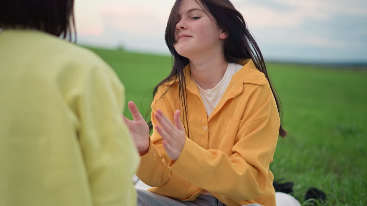 Ung kvinde mediterer på grøn eng iført gul jakke, lukkede øjne og trækker vejret roligt, reflekterende stilling og centreret tilstedeværelse, blød aftenhimmel, fredfyldt naturlyd, blid grounding