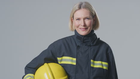 studio portrait of smiling mature female firefighter against plain background