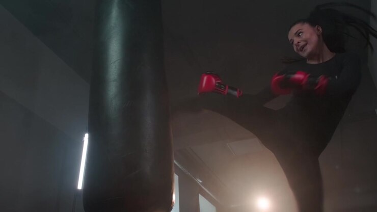 Giovane donna che si allena nel kickboxing con un sacco da boxe in palestra