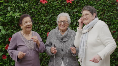 portrait of diverse elderly women dancing happy enjoying celebrating retirement listening to music together in outdoors garden