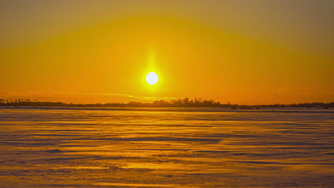 static time lapse view of an empty snow covered field on a horizon with a soothing setting sun with golden glow and clear skies