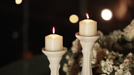 two white candles glowing softly in dim light, surrounded by delicate white flowers