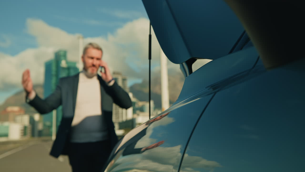 A man is talking on the phone near his car in the city