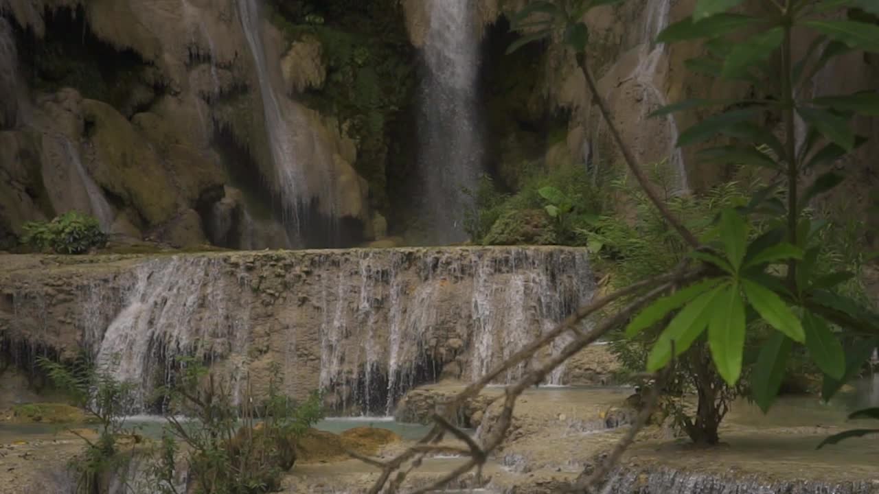 clip de cámara lenta en una pequeña cascada con hojas verdes frente a la cámara