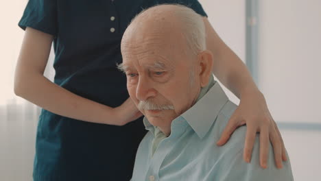 portrait of emotional sad elderly man, caring nurse cheering up