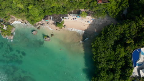 Ascending-aerial-view-of-people-on-the-sand-beach-in-Bali-surrounded-by-luxury-tropical-resorts