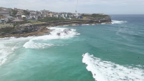 surfers on foamy rolling waves of tamarama beach with tamarama point in eastern suburbs, sydney, new south wales, australia