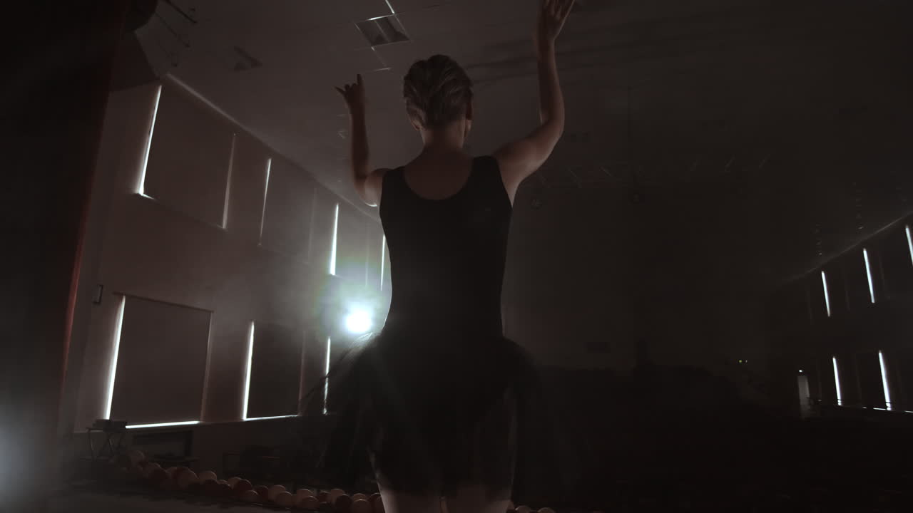 슬로우 모션: 무대 위의 프리마 발레가 콘트라의 어두운 빛 속에서 공연을 연습합니다.