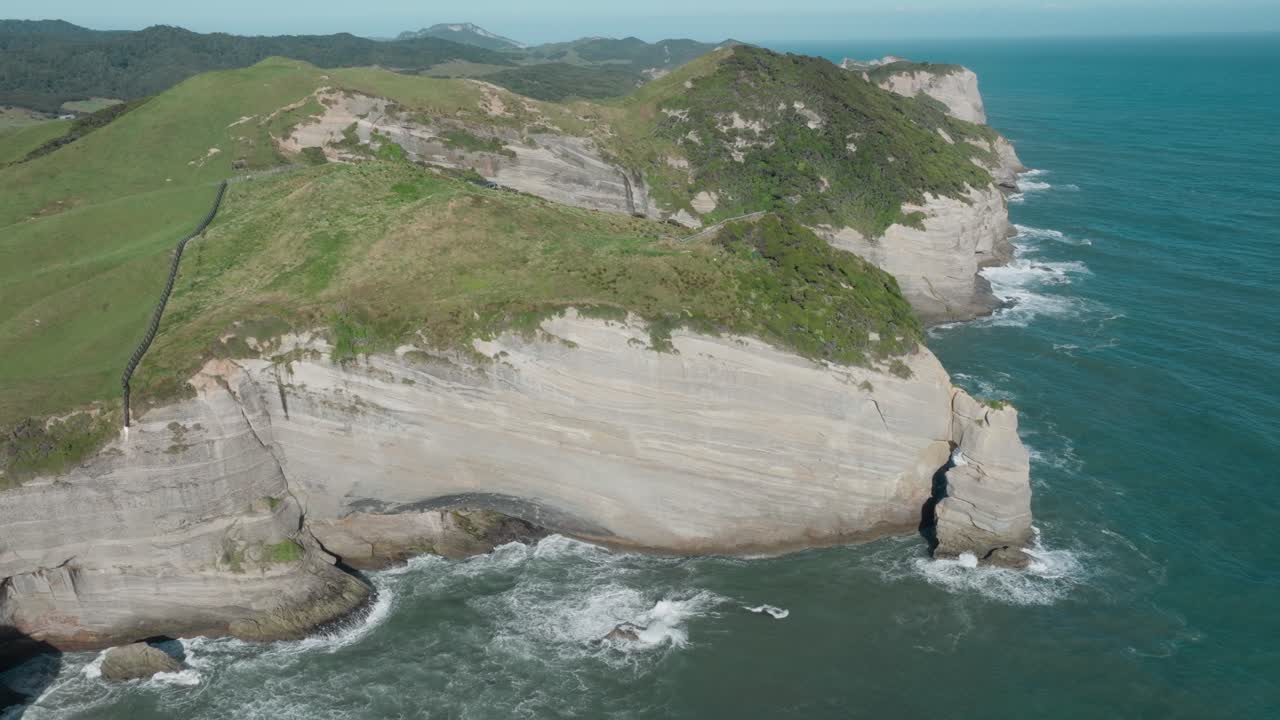 impresionante vista aérea que se eleva sobre el remoto desierto paisaje costero del cabo de despedida promontorio con olas violentas y salvajes del océano rompiendo contra los acantilados en nueva zelanda aotearoa