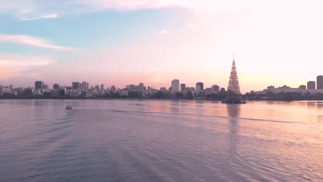 Panorámica-De-Izquierda-A-Derecha-Que-Muestra-El-árbol-De-Navidad-Flotante-Más-Alto-Del-Mundo-De-2018-En-Río-De-Janeiro-Con-Una-Lancha-Rápida-Y-Un-Esquiador-Acuático-Que-Pasan-Al-Atardecer