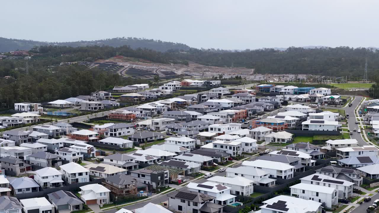 Drone glides over contemporary suburban homes, mountain backdrop, overcast daylight, steady wide-angle shot