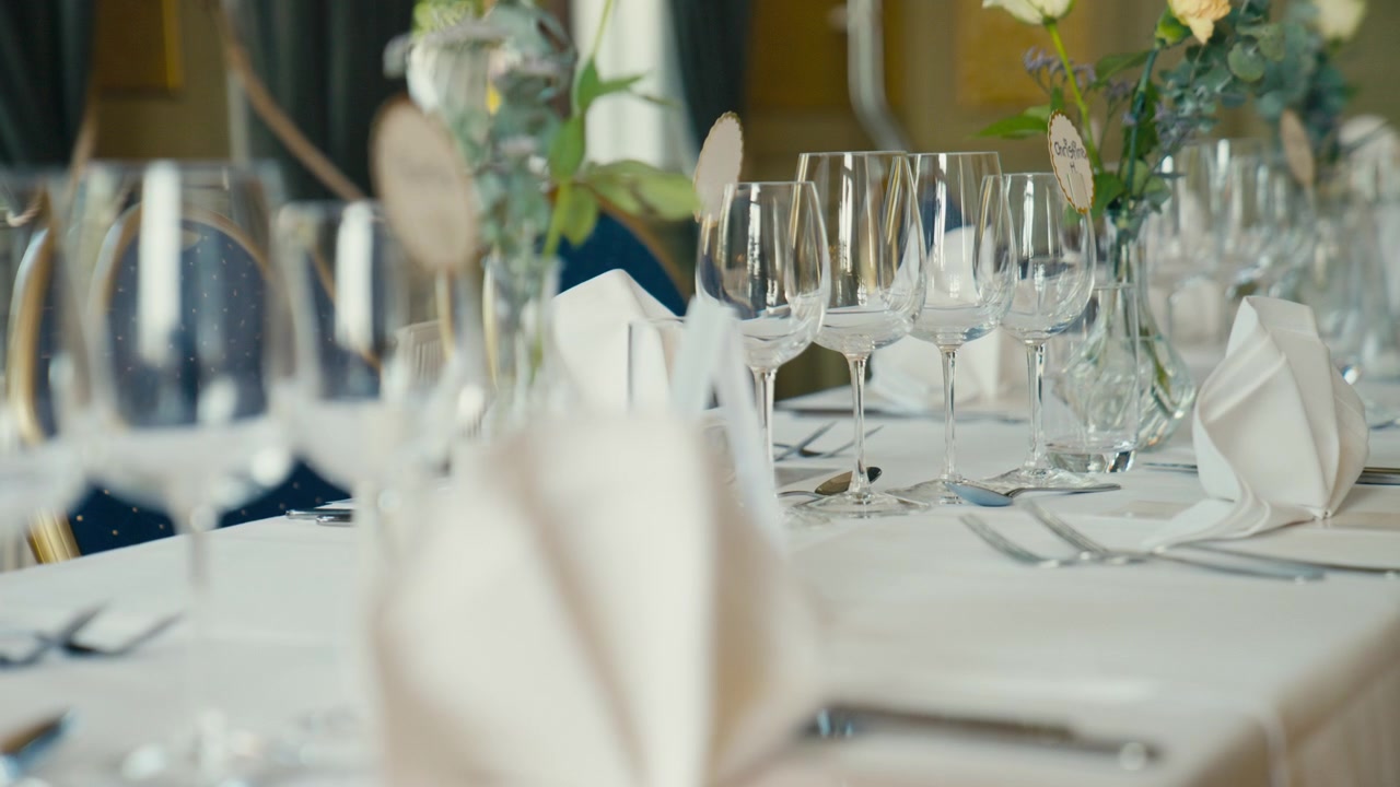 An elegantly arranged wedding reception table is set with glassware, folded napkins, floral details, and soft natural light, creating a refined atmosphere of celebration and formal dining.