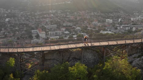 woman, boy, dog walking along wooden bridge over gorge mountain plateau covered forest. aerial view flight drone sunset. summer holidays. tourism. family walk. national park, ovech, provadia, bulgaria