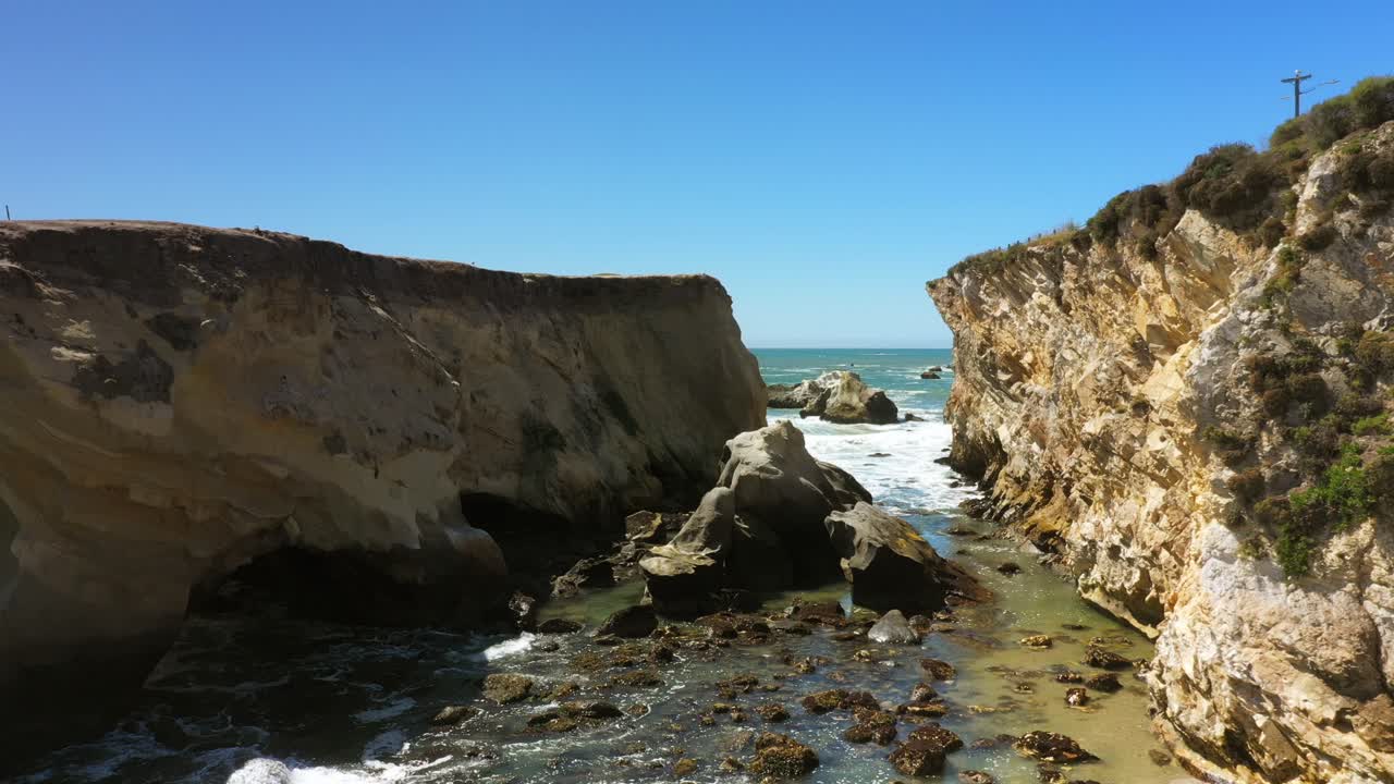 Tidal seawater between two cliffs with waves rolling in along the Pacific coast - aerial push in flyover in slow motion