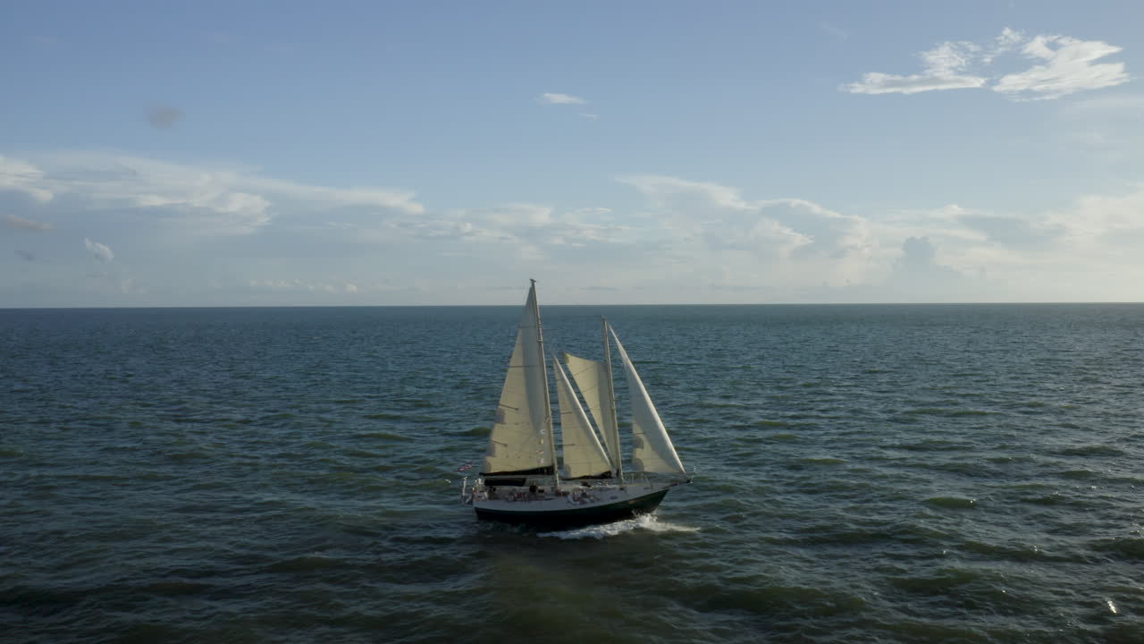 A graceful sailing yacht cuts across the shimmering sea with sails fully extended beneath a wide blue sky, evoking freedom, leisure, and timeless nautical adventure