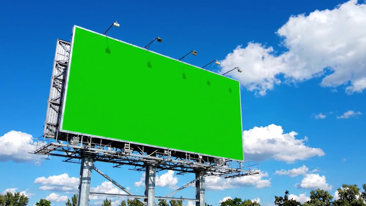 Et levende grønt reklameskilt mod en klar blå himmel med bløde skyer, der fremviser et blankt lærred for reklame og kreativitet i et åbent landskab.