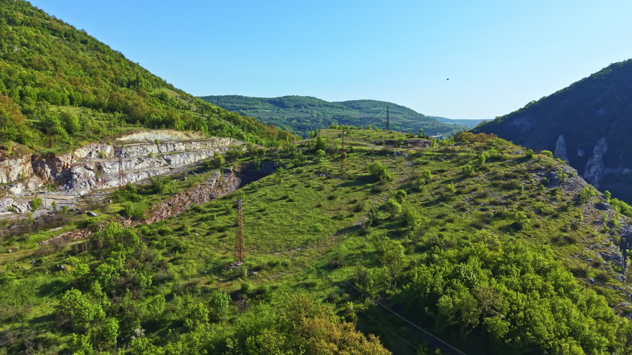 Vedute di una collina verde con alberi e montagne distanti durante il giorno sotto un cielo azzurro e limpido