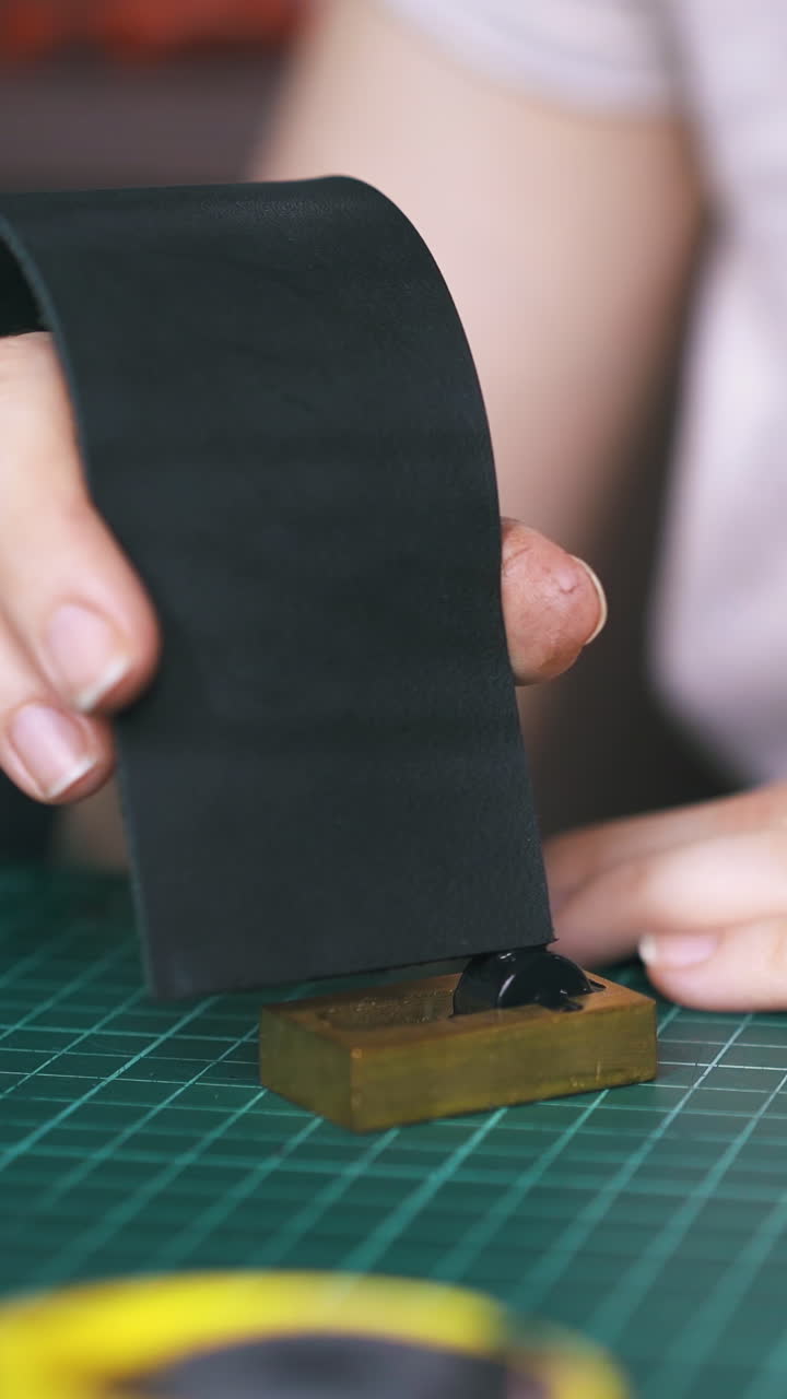 CU: Professional designer colours leather strip edge with black paint in pure copper on green cutting mat closeup