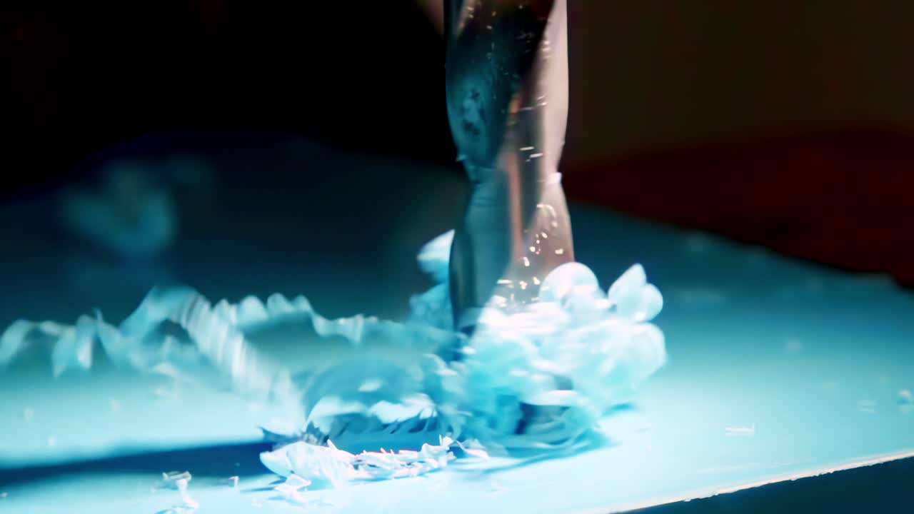 An extreme close-up, slow-motion shot shows a metal drill bit boring a hole into a sheet of blue plastic, sending beautiful curly shavings spiraling upwards from the surface