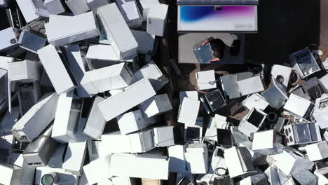 man throws old electrical appliances onto junk pile from back of truck, aerial