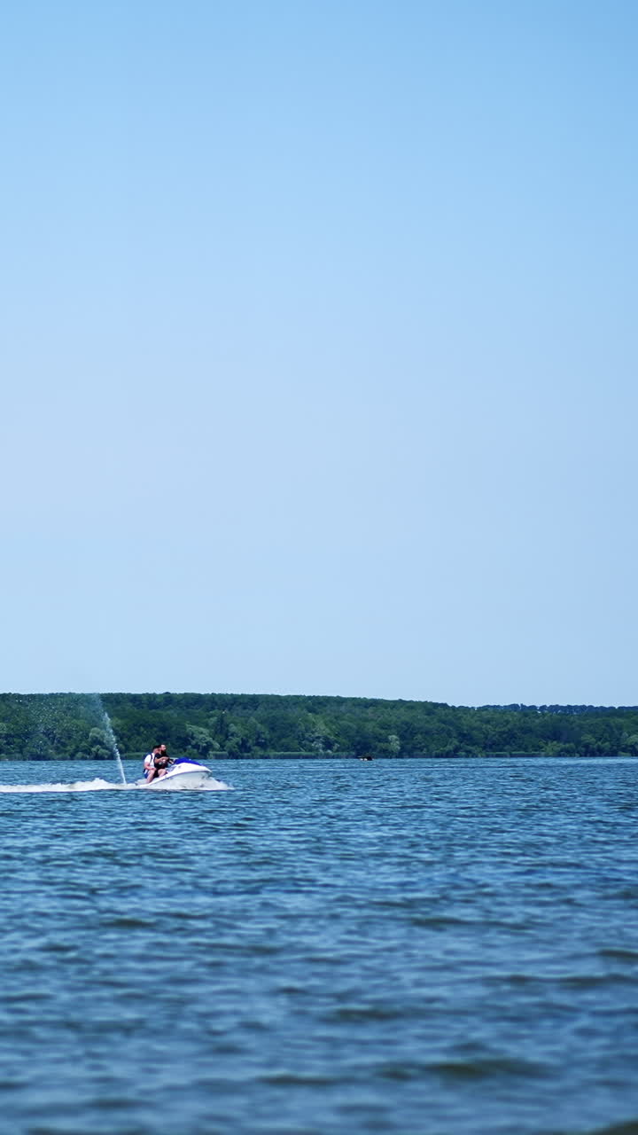 People riding jet ski water bike on the river on sunny day. Two water bikers slowly approaching the waterfront. Vertical video