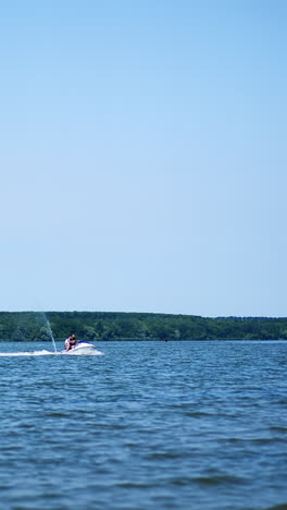 people riding jet ski water bike on the river on sunny day. two water bikers slowly approaching the waterfront. vertical video