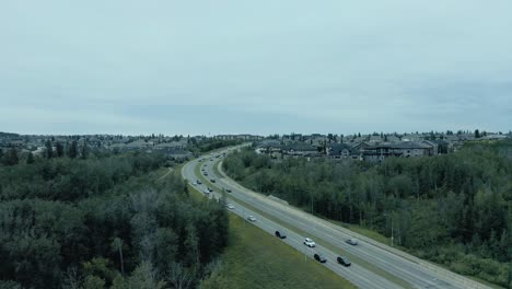 aerial pan left. horizon with cookie cut mega homes. highway freeway in between residential community. with lush green forests sourounding the homes. light traffic. buttery smooth aerial pan left.