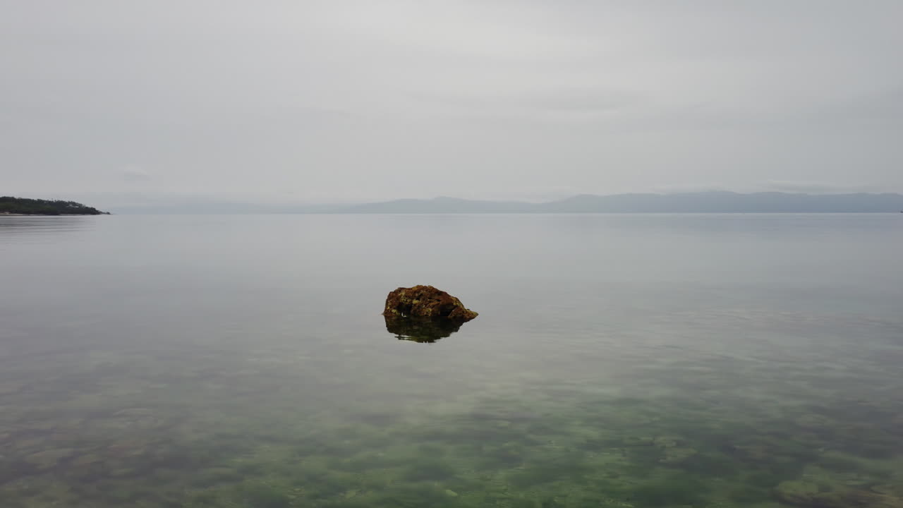 Slow revealing drone shot of a rock in the ocean and houses, a forest and the shore in the back, Aerial, Cinematic, Cebu, Philippines, Asia