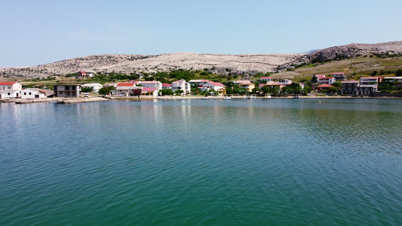 aerial slow motion landscape of Pag Island coastline lined with waterfront homes on a sunny summer day