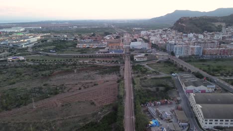 tracking shot of a train moving through farm fields and industrial areas, approaching a city at dusk