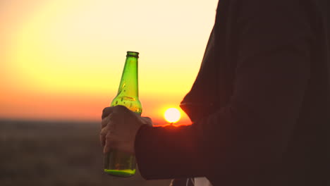 close up of a man drinking beer at sunset standing on the roof of a building against the background of a beautiful evening city.