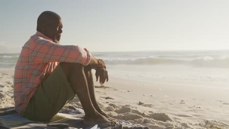 senior african american man wearing shirt and sitting on sunny beach