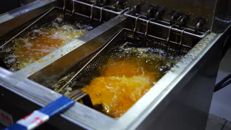 cook putting meat in deep fryer in commercial kitchen, close up