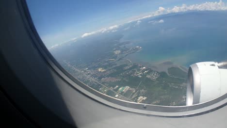 airplane flying over an island revealing a city and clouds in the horizon