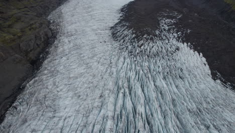 aerial tilt up glacier in iceland flowing down mountain between two ridges