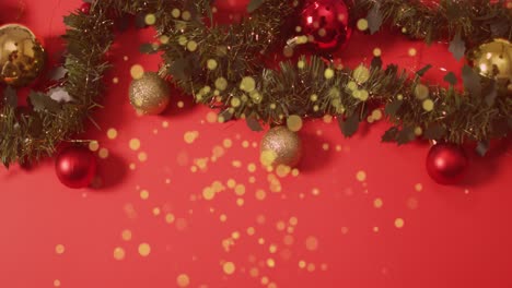 Animation-of-golden-dots-falling-over-red-background-with-christmas-decorations