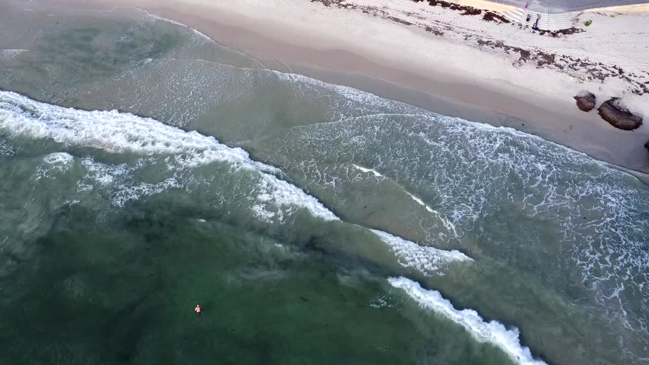 vista aérea de alto - las olas del océano índico y el nadador solitario en la playa de cottesloe, wa