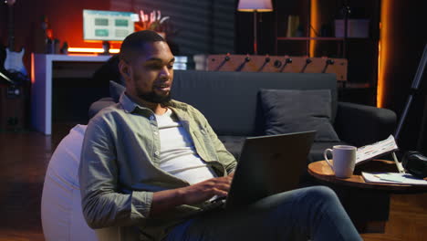 vertical video adult guy typing on laptop laying on couch at his stylish loft space