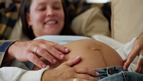 close up of a happy brunette woman with her husband stroking her pregnant belly during her pregnancy at home in a modern apartment