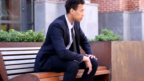 serious african businessman coming and sitting on bench