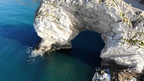 aerial over limestone durdle door arch surrounded by calm turquoise waters